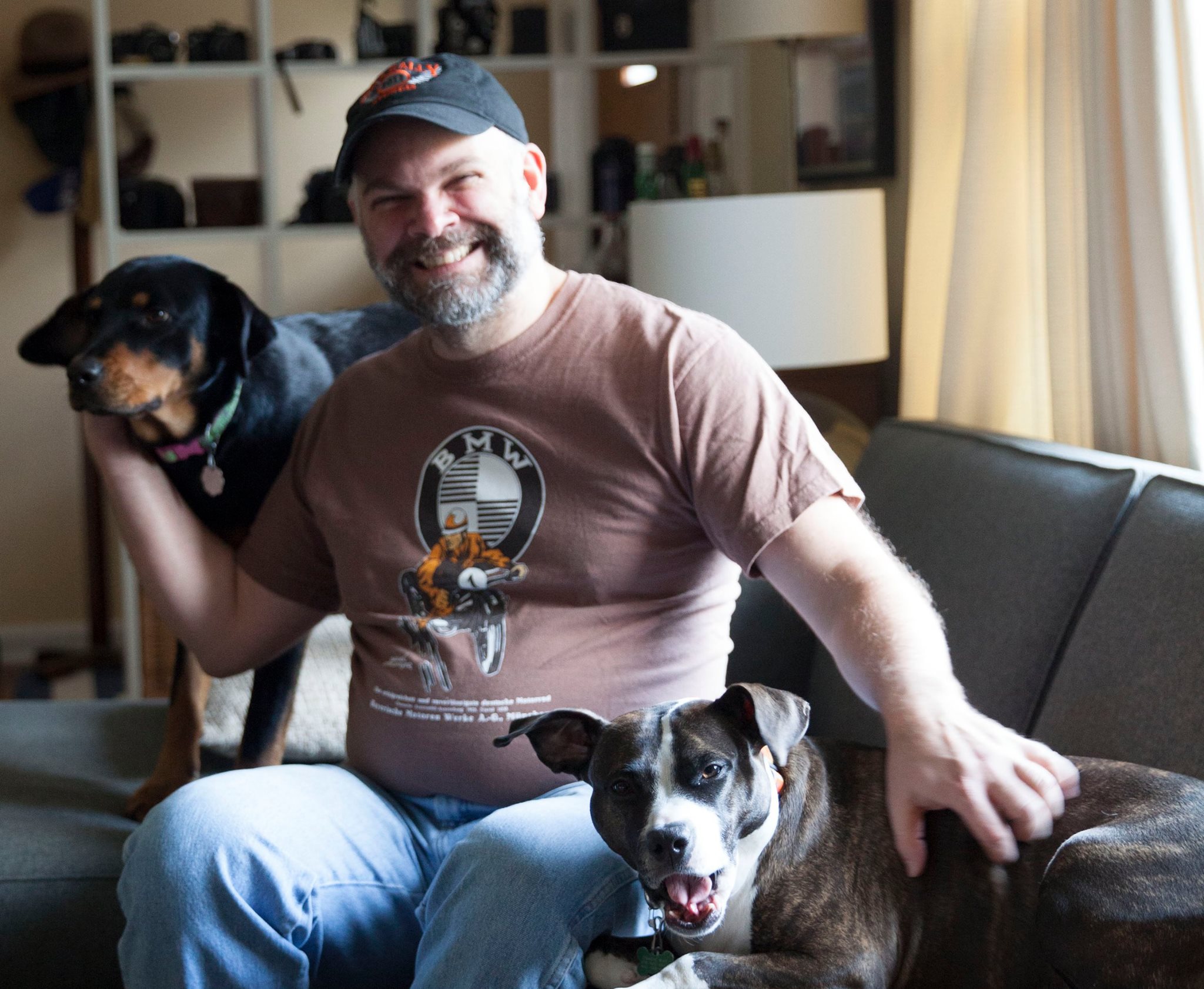 Photo of JP sitting on his couch with pups: Gracie (yawning) and Pearl